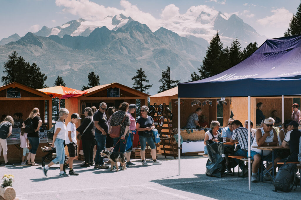 Besucherinnen und Besucher schlendern über den Moosalp Markt mit Blick auf eindrucksvolle Berggipfel und Alpenpanorama.