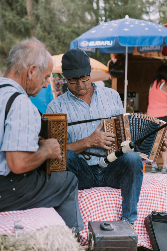 Zwei Musiker spielen traditionelle Handorgeln auf dem Moosalp Markt, umgeben von festlicher Marktstimmung.